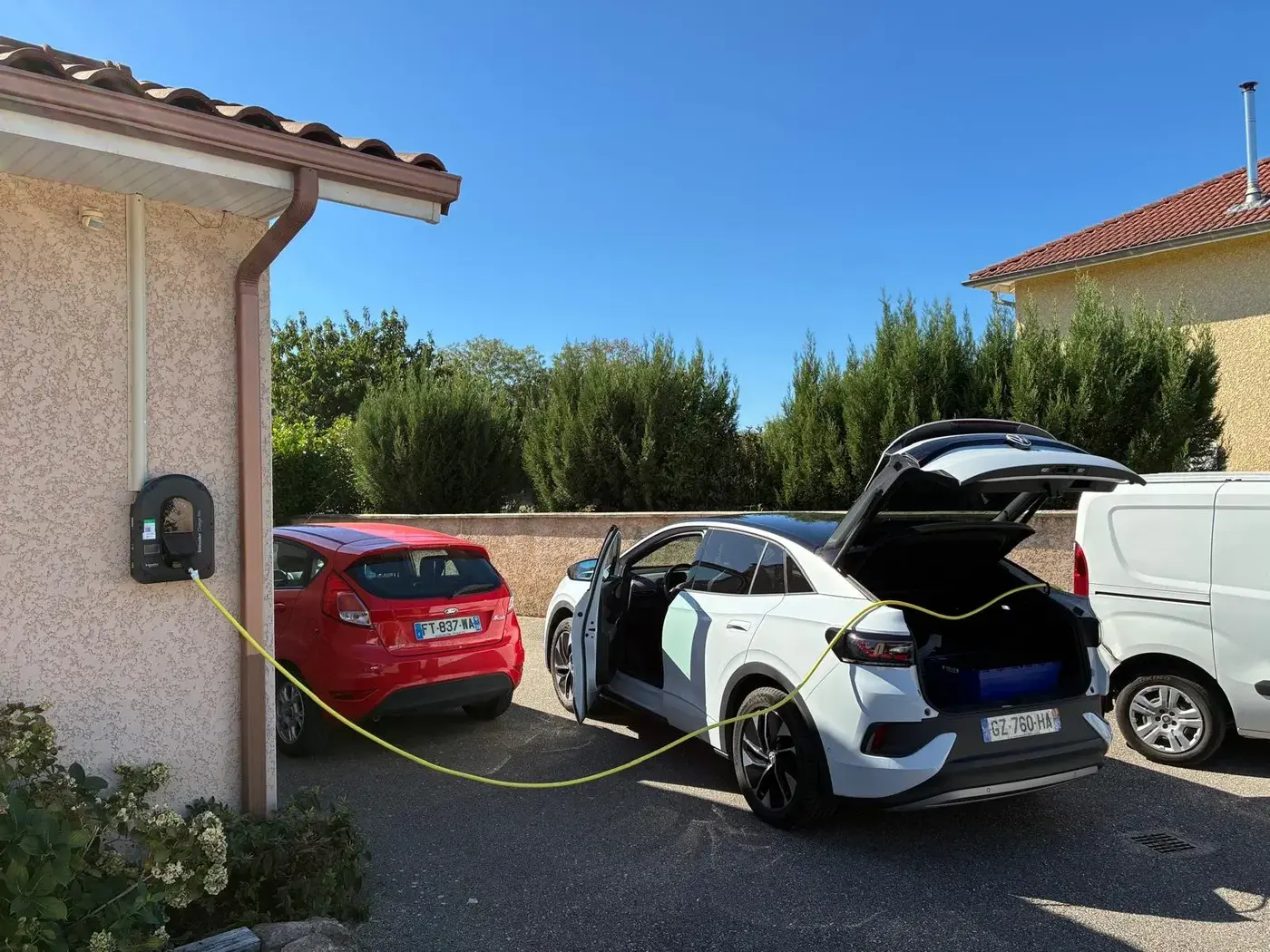 Borne de recharge murale installée chez un particulier, voiture électrique en charge